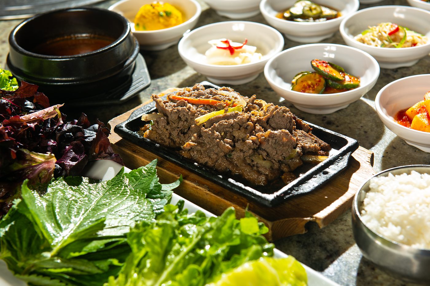 Bulgogi on a hot plate with lettuce wraps, banchan and rice at Woonamjung
